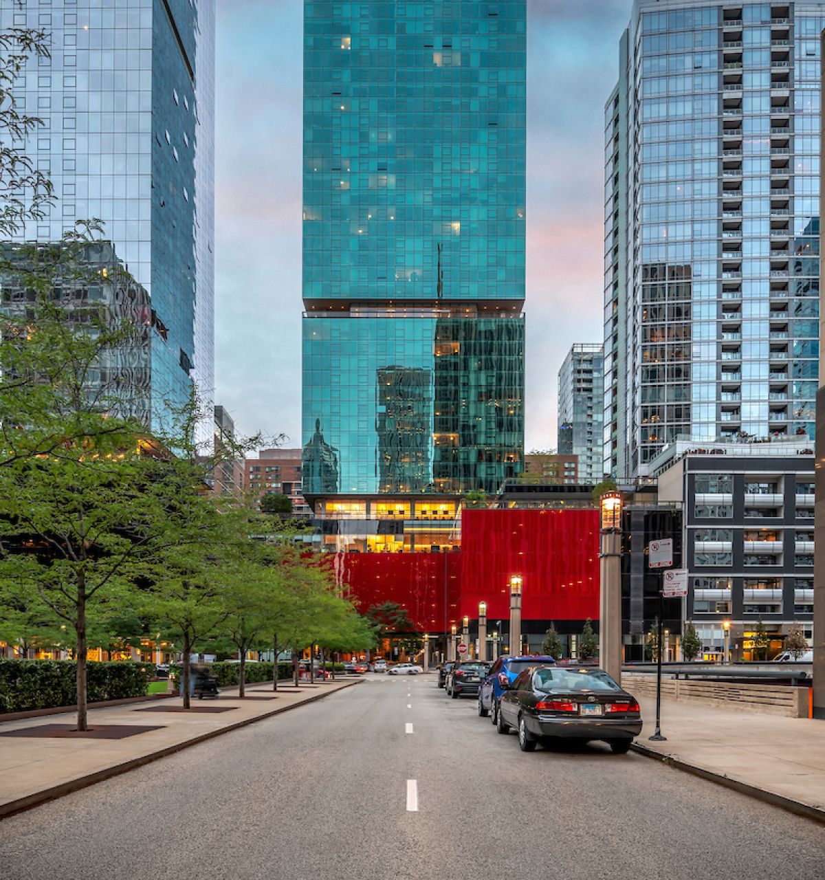 Optima Signature in Downtown Chicago with Tall glass skyscraper with red lower facade on a city street at dusk, flanked by other modern buildings.