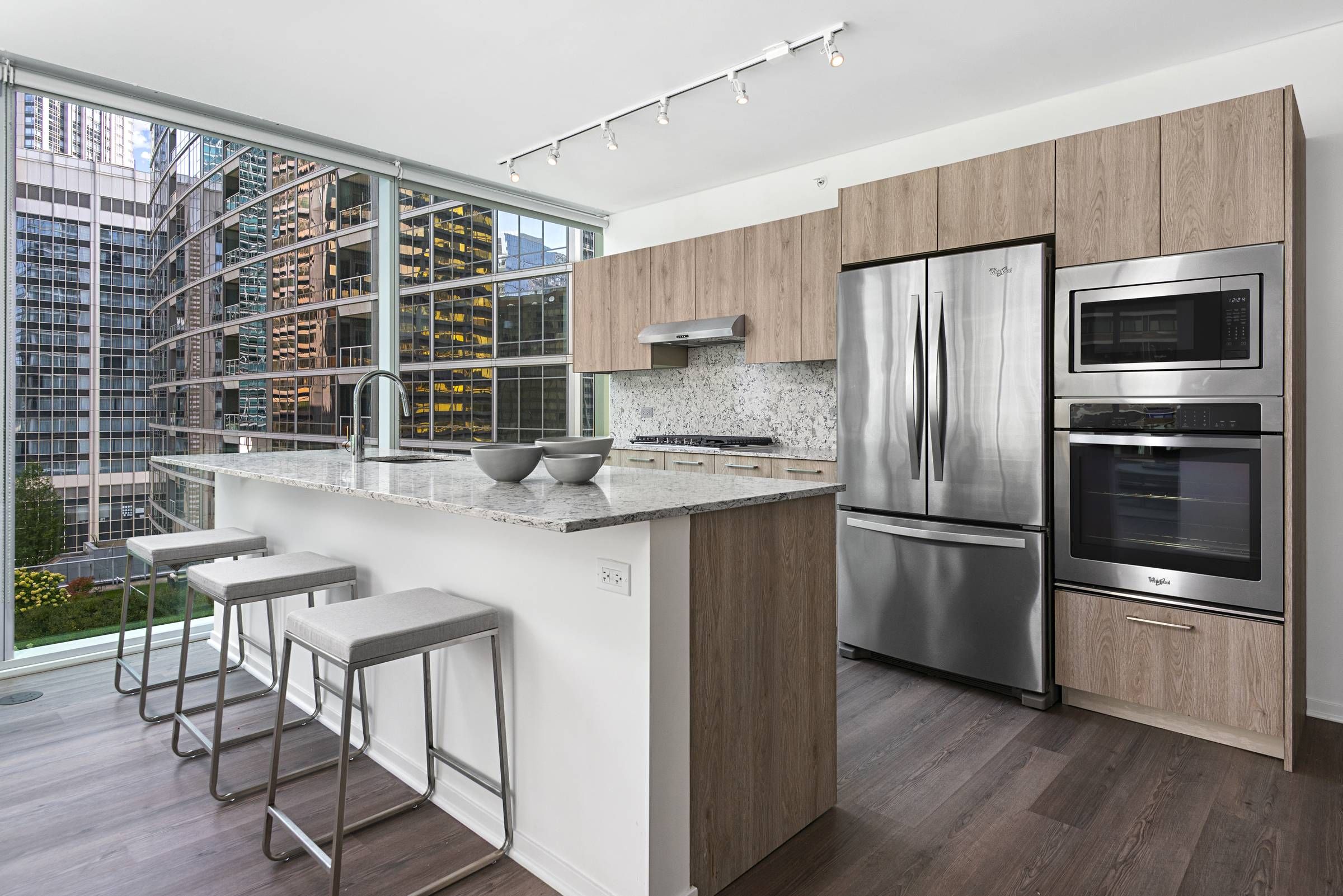 Optima Signature in Downtown Chicago with Modern kitchen with wood cabinets, stainless steel appliances, and floor-to-ceiling windows overlooking city buildings.