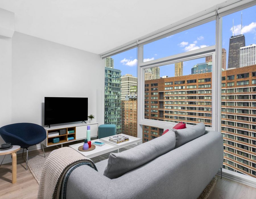Optima Signature in Downtown Chicago with Modern living room with a gray sofa, TV, and large windows showing a city skyline with tall buildings.