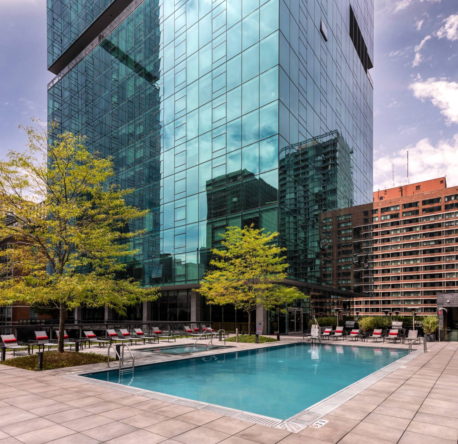 Optima Signature in Downtown Chicago with Outdoor pool with lounge chairs and trees beside a modern glass high-rise building in the city.