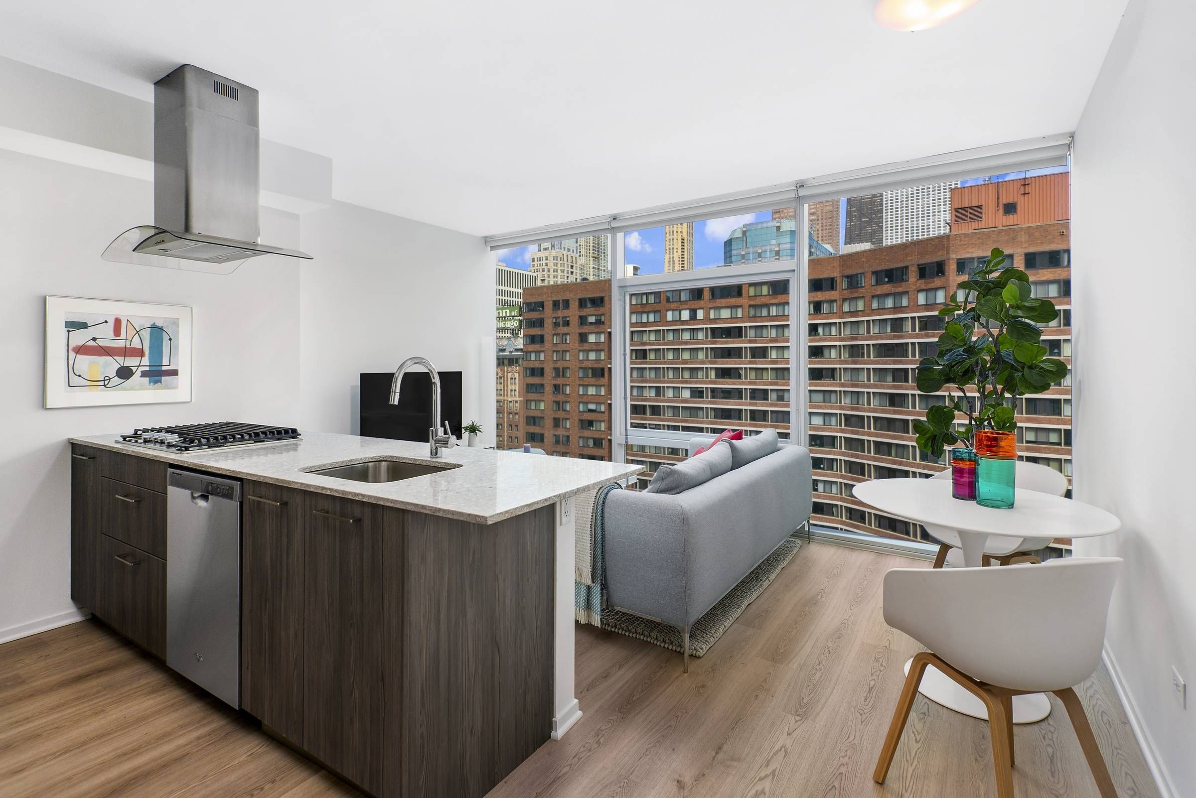 Optima Signature in Downtown Chicago with Modern apartment kitchen and living area with floor-to-ceiling windows overlooking city buildings.